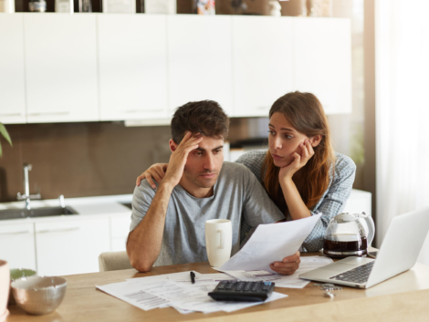 Depressed young Caucasian couple calculating family budget in kitchen, trying to find a way to make both ends meet, having stressed and frustrated looks: caring wife embracing her unhappy husband